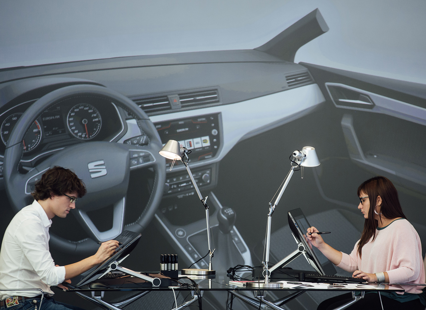Deux nouveaux concepteurs de voitures dessinent sur des écrans électroniques avec une photo de l'intérieur d'une voiture en toile de fond - SEAT Ressources Humaines