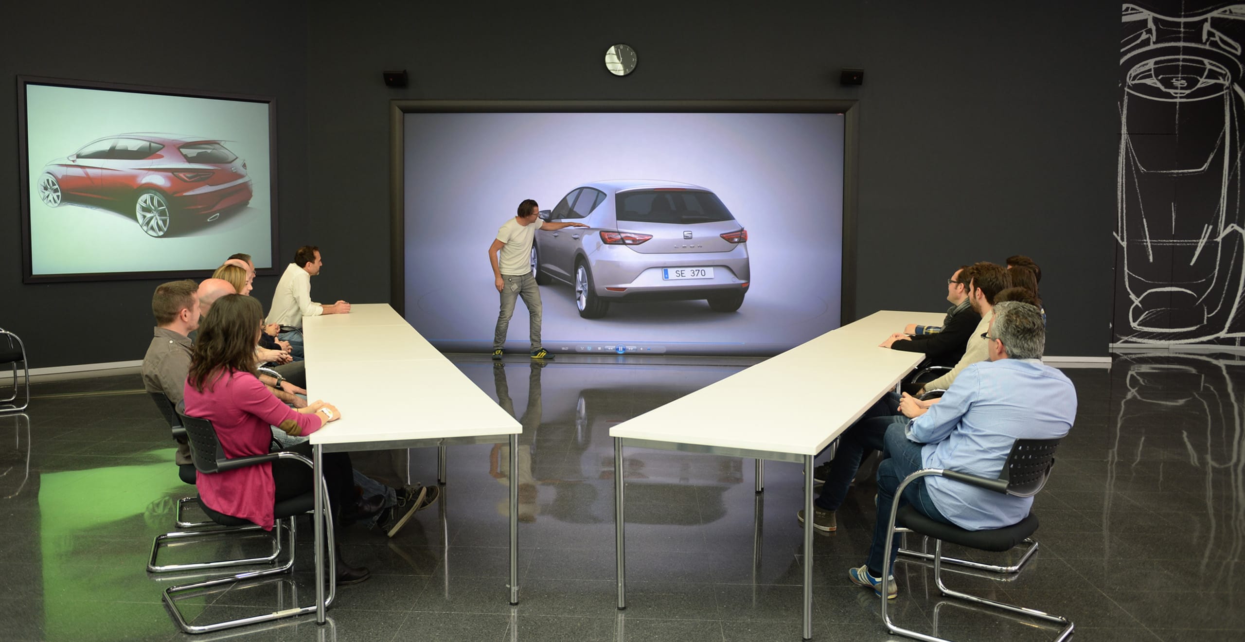 Table ronde avec un homme montrant du doigt la conception automobile SEAT Leon avec un groupe de personnes assisent à une table - SEAT Ressources Humaines