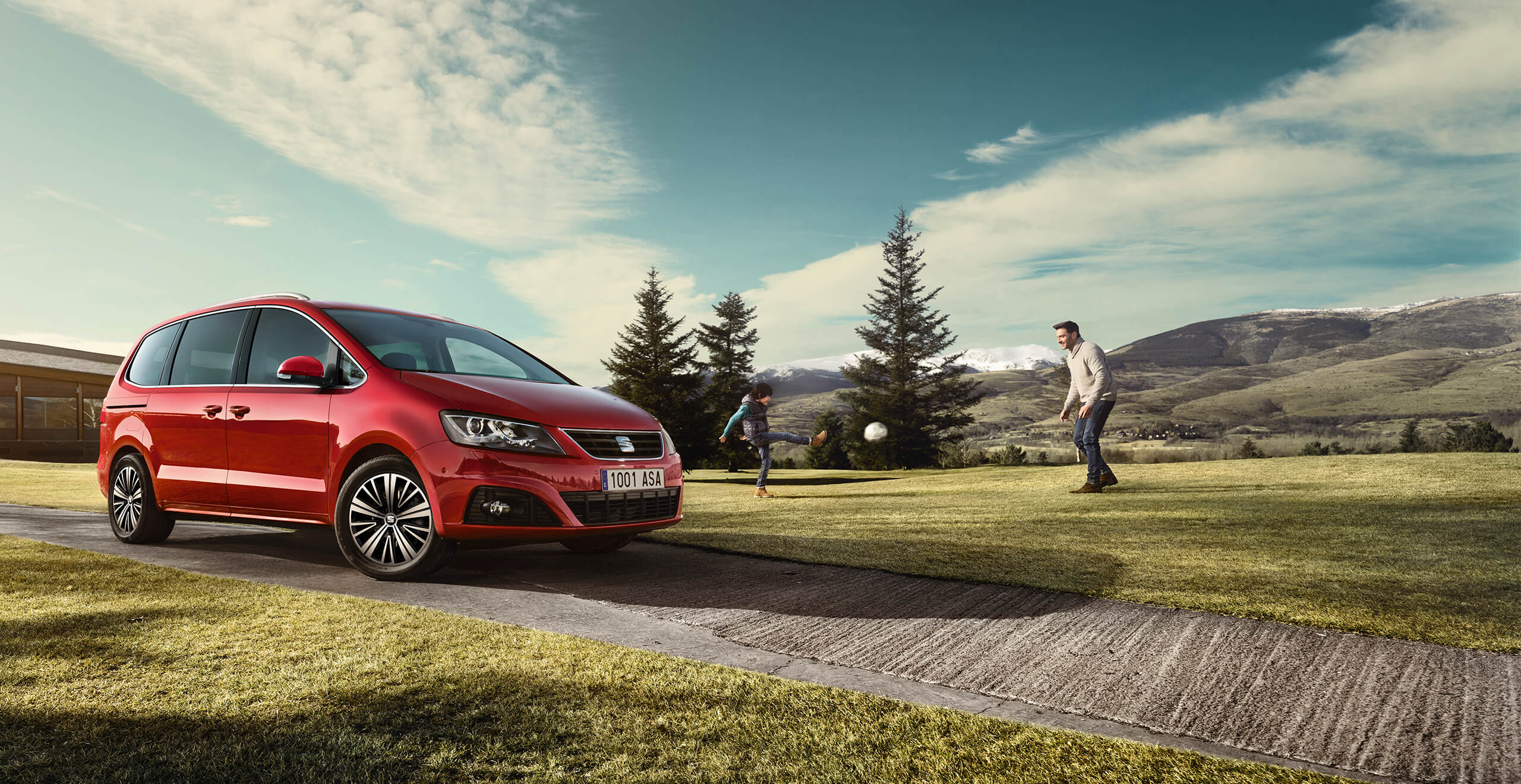 SEAT services voitures neuves extension de garantie entretien - Vue panoramique d'une SEAT Alhambra 7 places MPV rouge avec deux personnes jouant au football derrière.