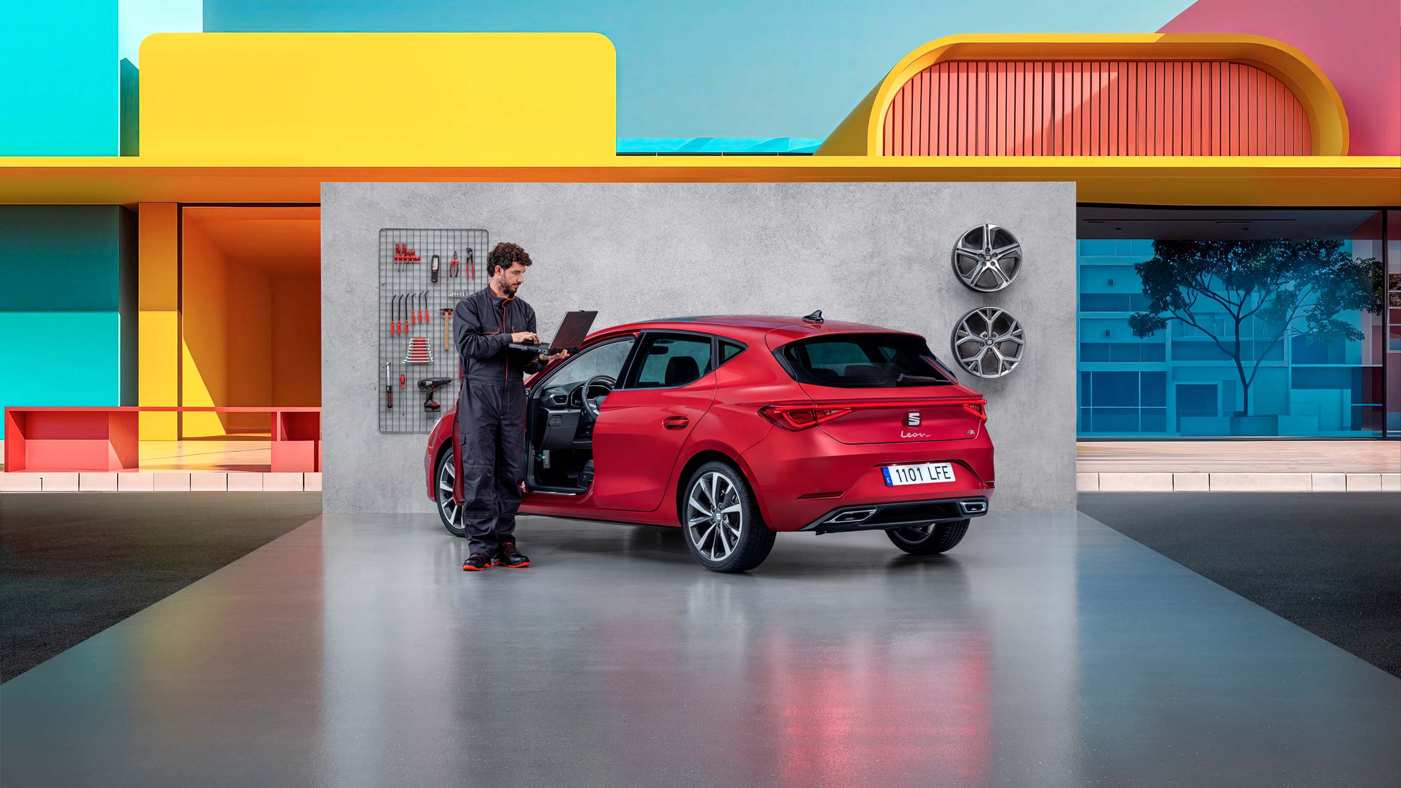 Technicien automobile utilisant un outil de diagnostic côté d'une SEAT Leon rouge, portière ouverte, dans un atelier d’entretien.