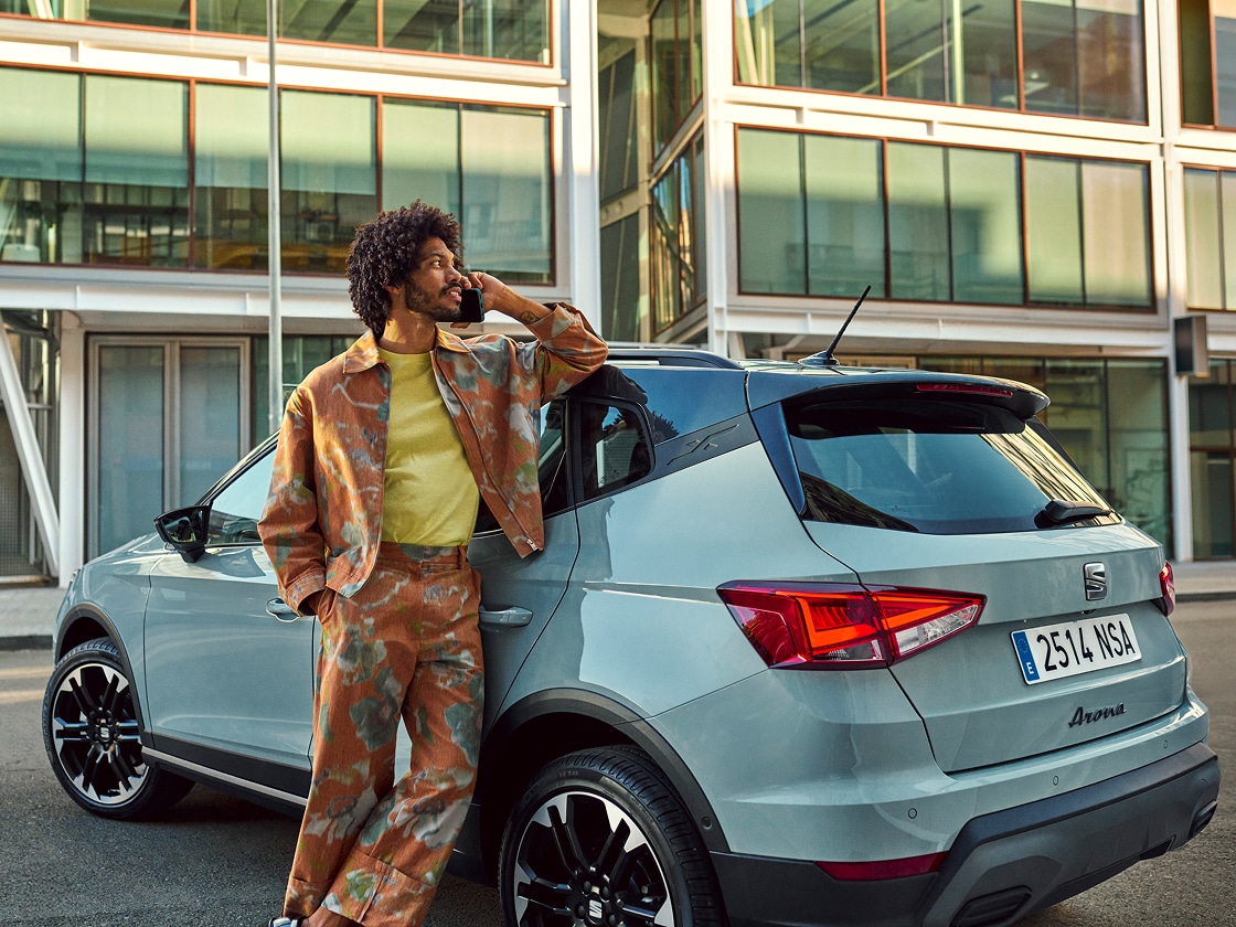 SEAT Arona garée devant un bâtiment moderne avec une personne  appelant l'assistance routière.  