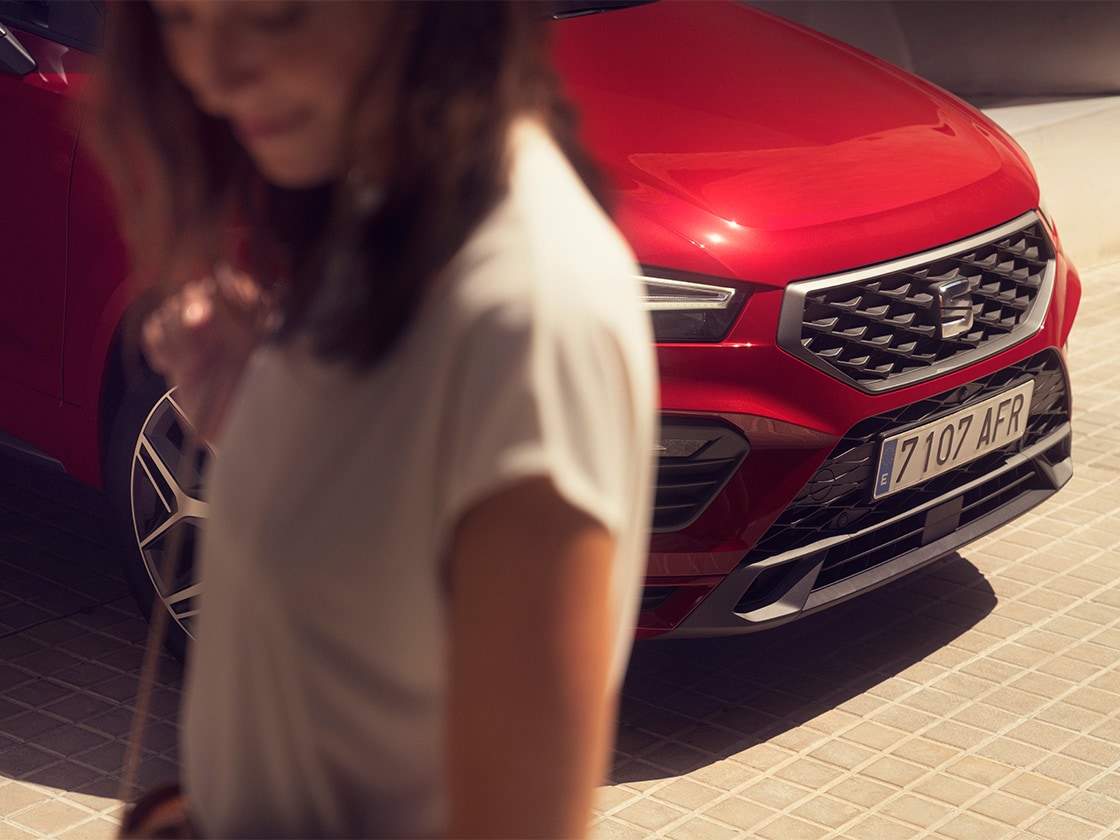 vue avant d’une seat ateca rouge garée en plein soleil. Une femme se tient à côté de la voiture.