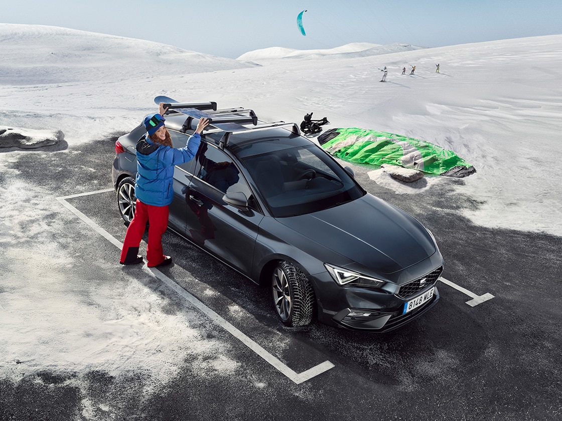 Une SEAT Leon garée en extérieur dans un village de montagne avec une personne avec une tenue de montagne utilisant les galeries de toit.