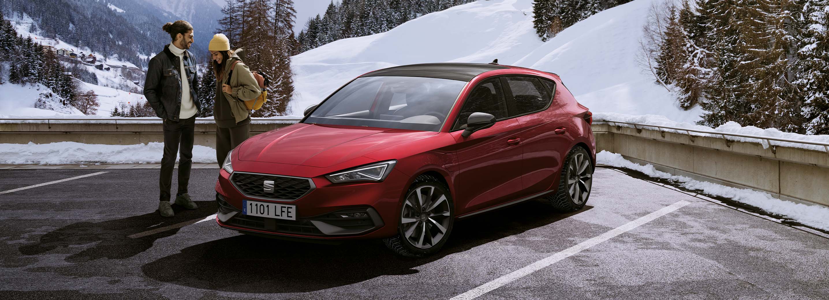Deux personnes debout à côté d’une seat leon rouge, dans un décor extérieur enneigé, montrant que vous pouvez profiter des services seat partout, quelles que soient les conditions.