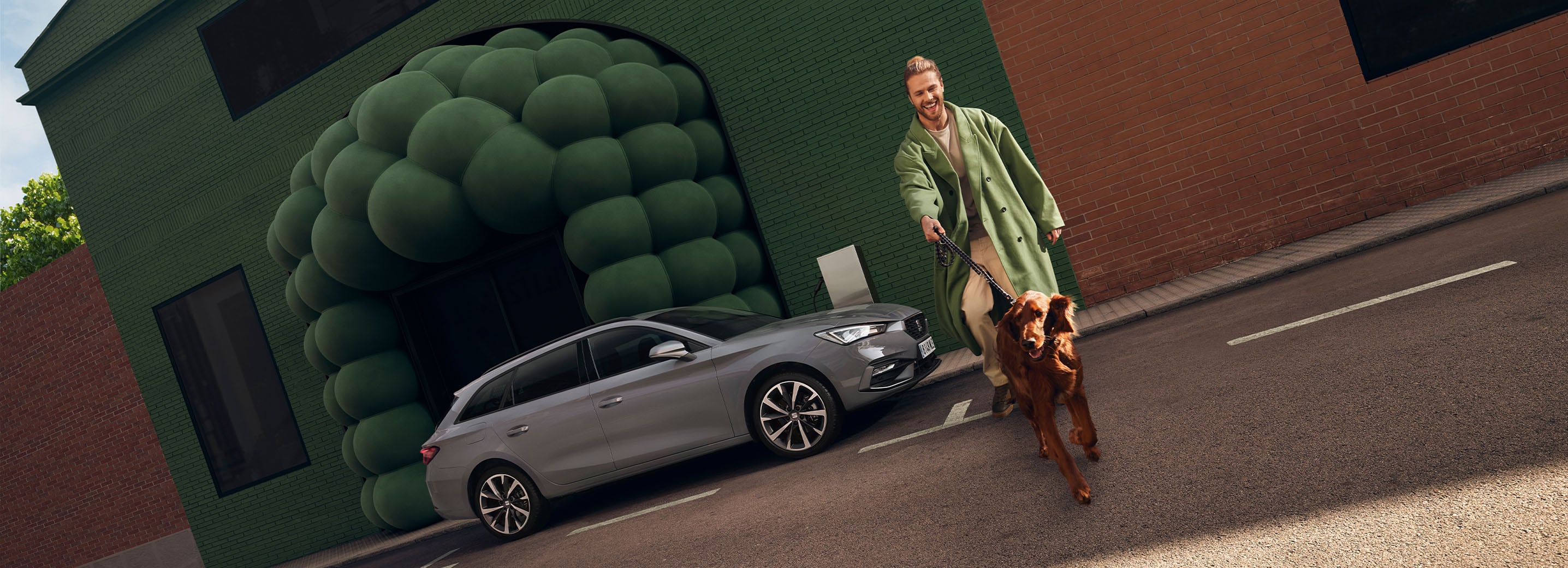 Une seat leon sportstourer grise avec des phares équipés de la fonction de clignotants dynamiques. Une personne passe à proximité, vêtue dans des tons assortis à l’arrière-plan.