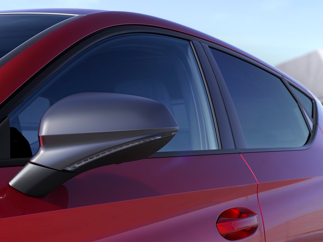 Vue latérale d’une SEAT Leon 5 portes rouge, garée en plein air sous un soleil éclatant, mettant en valeur les détails extérieurs du Pack FR.