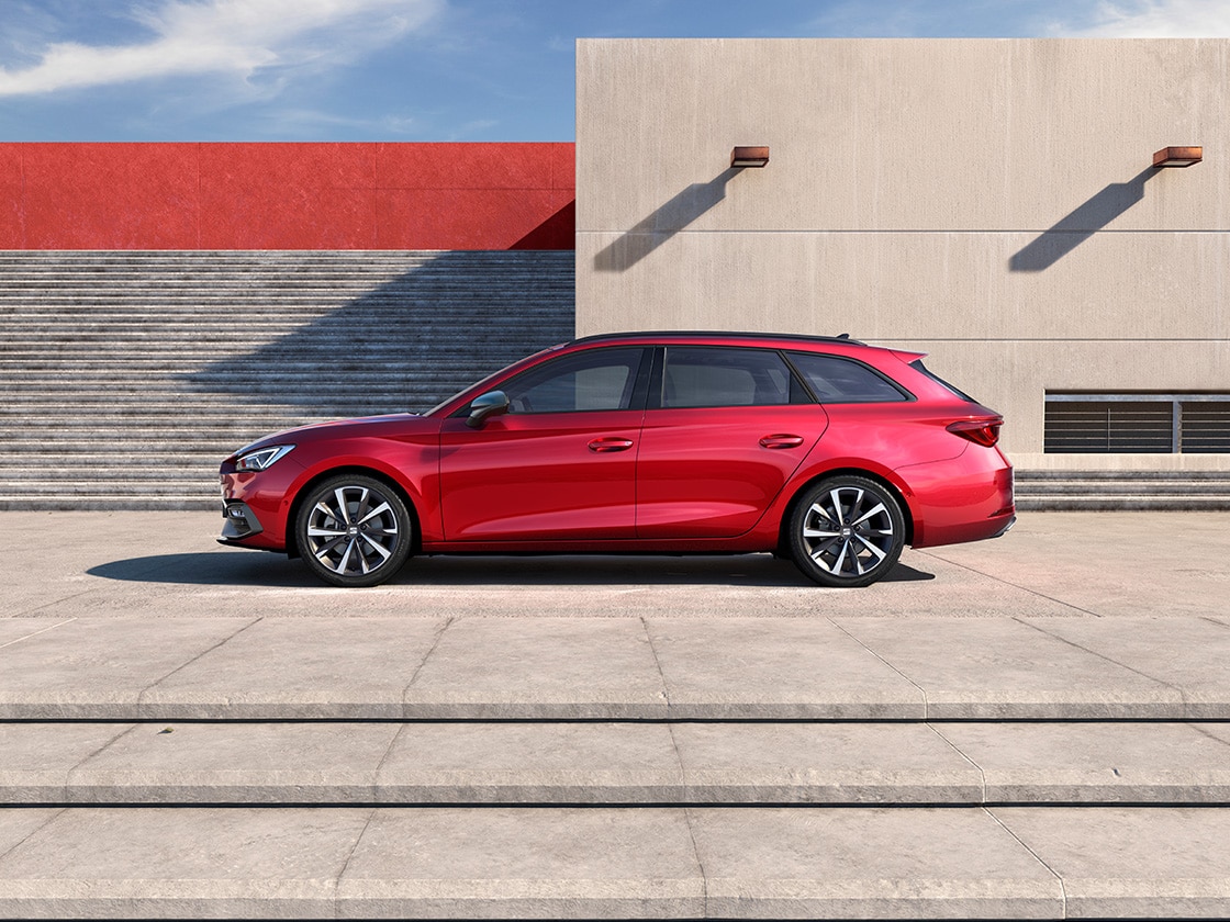 Une seat rouge stationnée dans un parking sombre, laissant passer un rayon de soleil qui éclaire la voiture et la personne qui se tient à ses côtés.