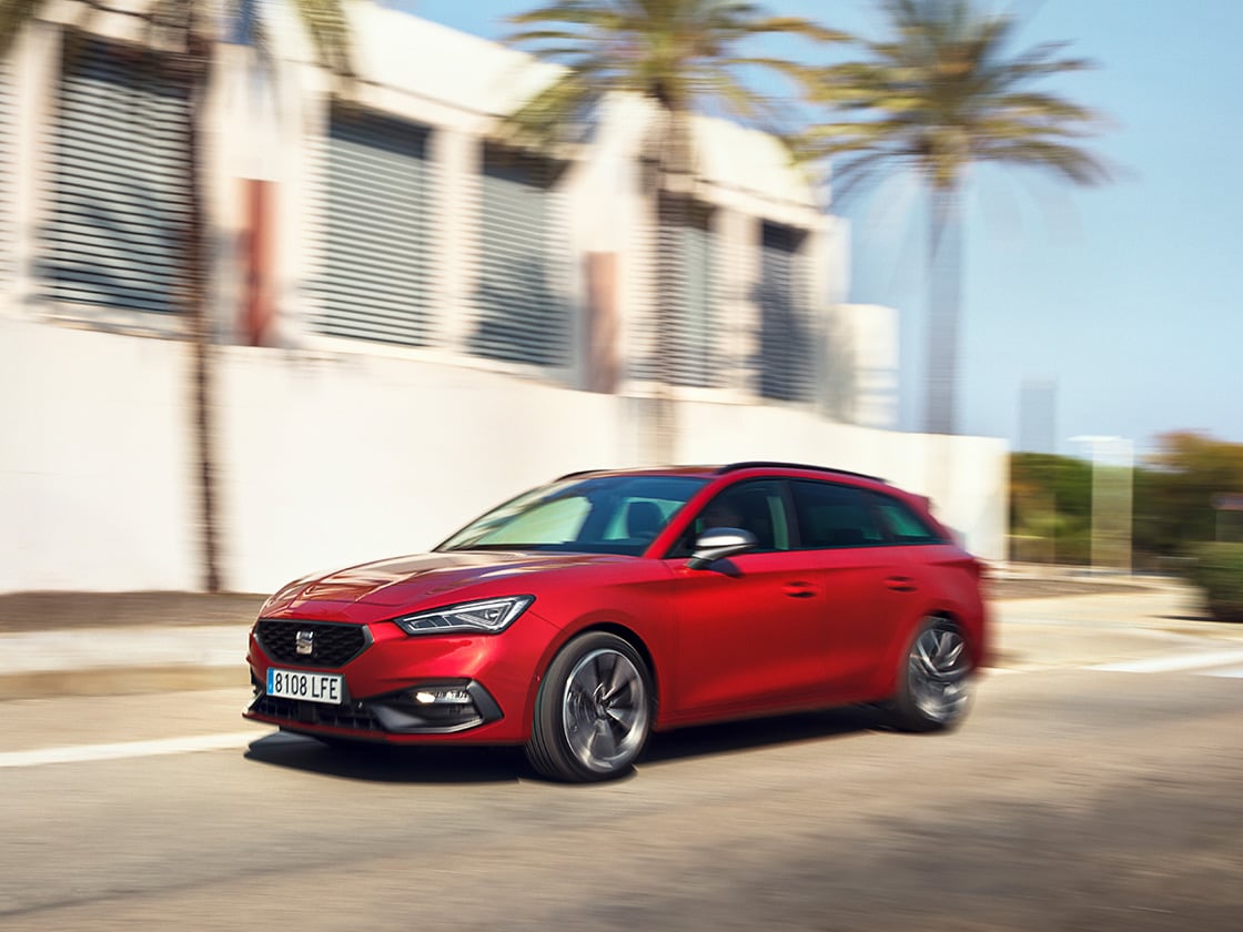 Une seat leon sportstourer rouge profite du plan de service et d’entretien SEAT, en mouvement dans un quartier résidentiel avec une maison et des palmiers.