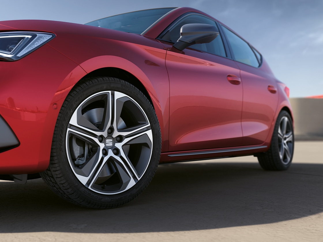 Une seat leon sportstourer rouge désir, mettant en valeur la baguette de protection des portières et les jantes en alliage, garée sous un ciel dégagé.