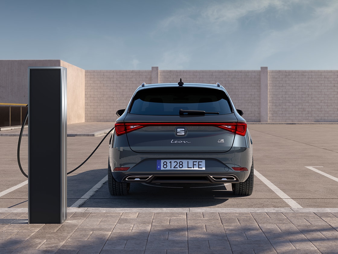 Vue arrière de la seat leon sportstourer fr en train de se recharger automatiquement à une borne, une nouvelle voiture à hayon pour 2025 en gris magnétique, équipée de capteurs de stationnement arrière et de phares et feux arrière led.