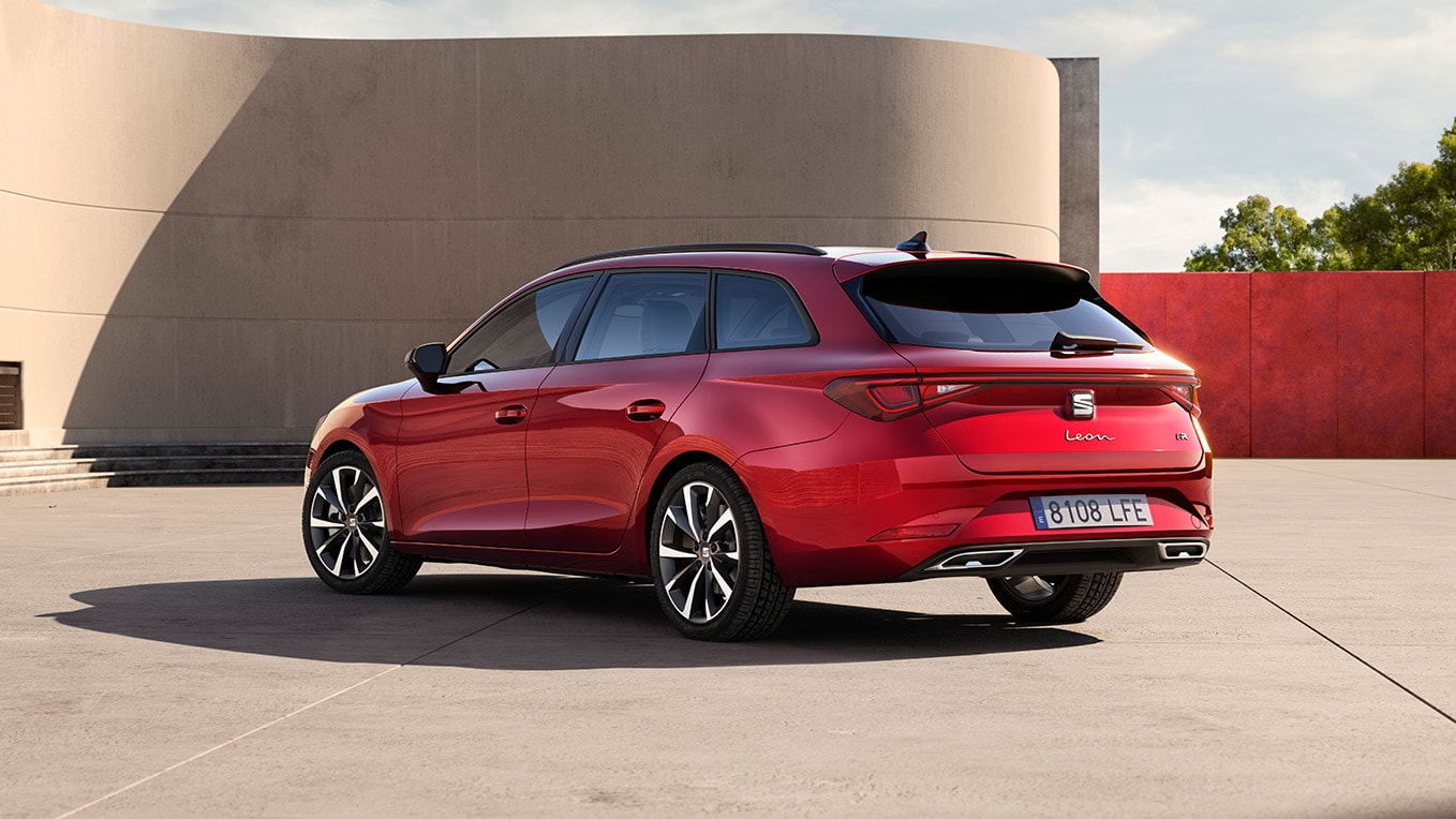 Vue arrière latérale du break seat. Seat leon sportstourer en rouge désir, stationnée face au mur d’un bâtiment en extérieur. Cette perspective met en valeur le design arrière du véhicule.