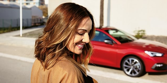 woman smiling near a red seat leon, highlighting the flexibility and convenience of hybrid vehicles in daily life.