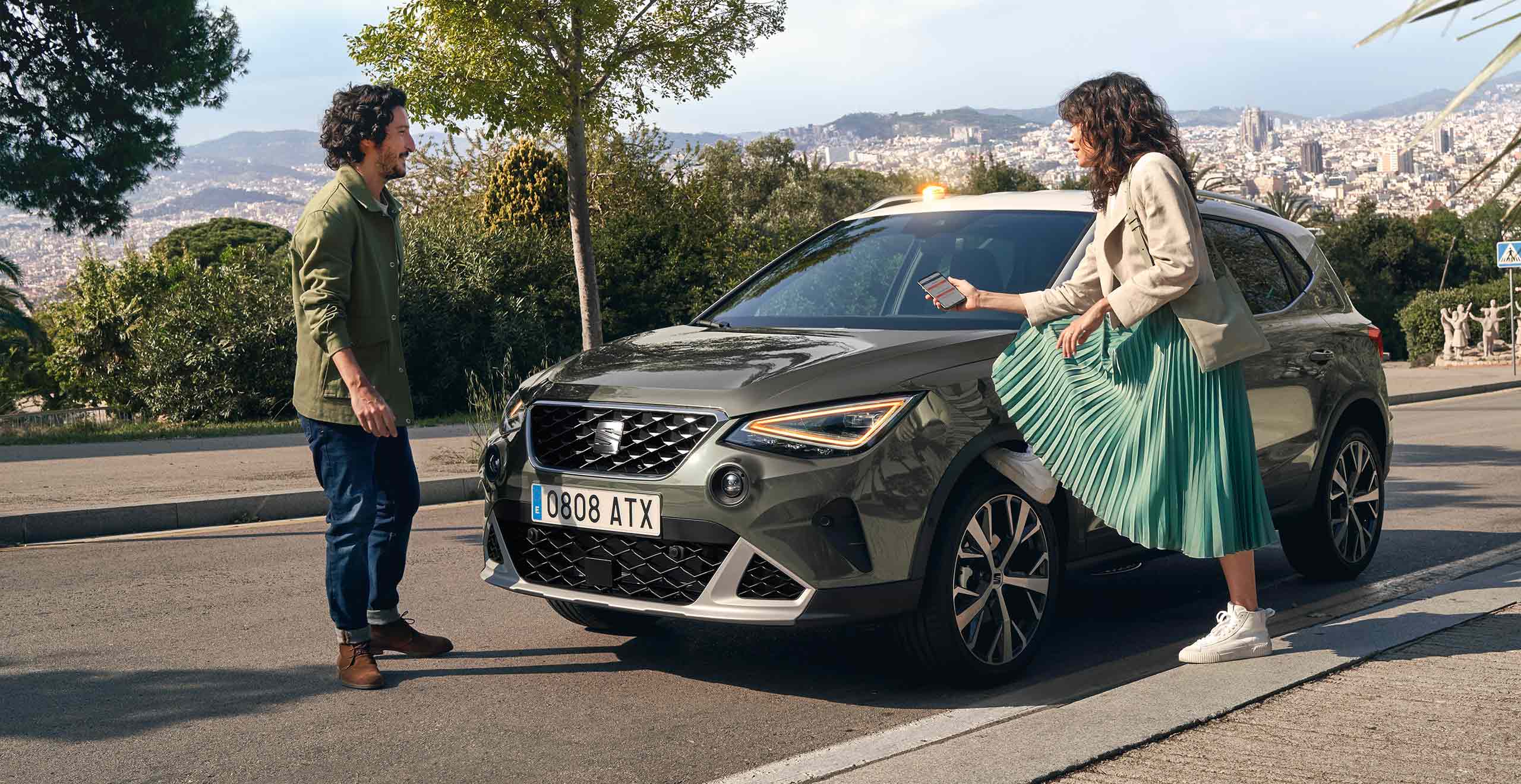 Femme avec son pied sur la roue de la SEAT Arona qui regarde son smartphone