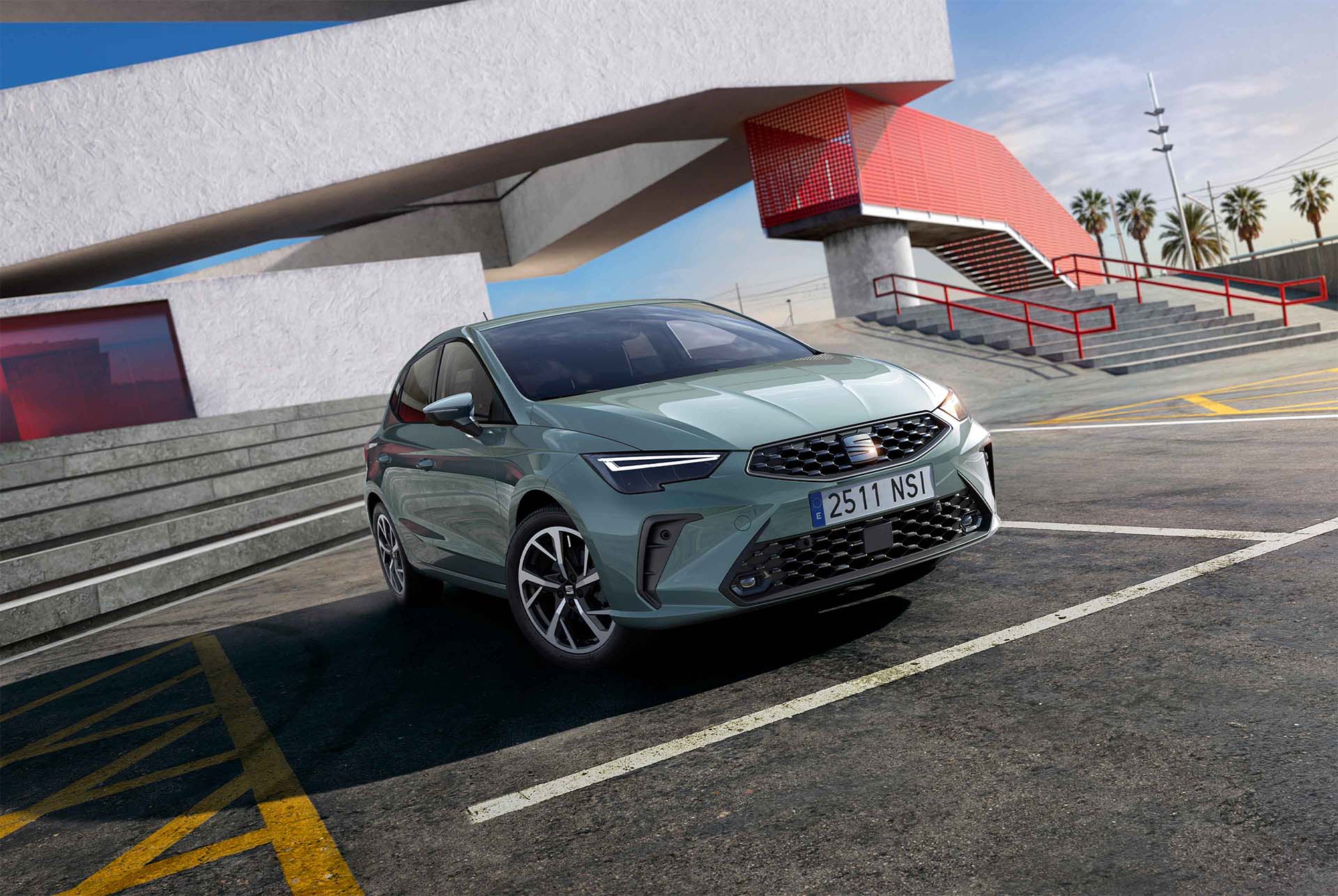 Vue d’une citadine SEAT Ibiza dans une teinte gris foncé, stationnée sur une place urbaine arborant des éléments architecturaux angulaires en béton, sous un ciel bleu dégagé.