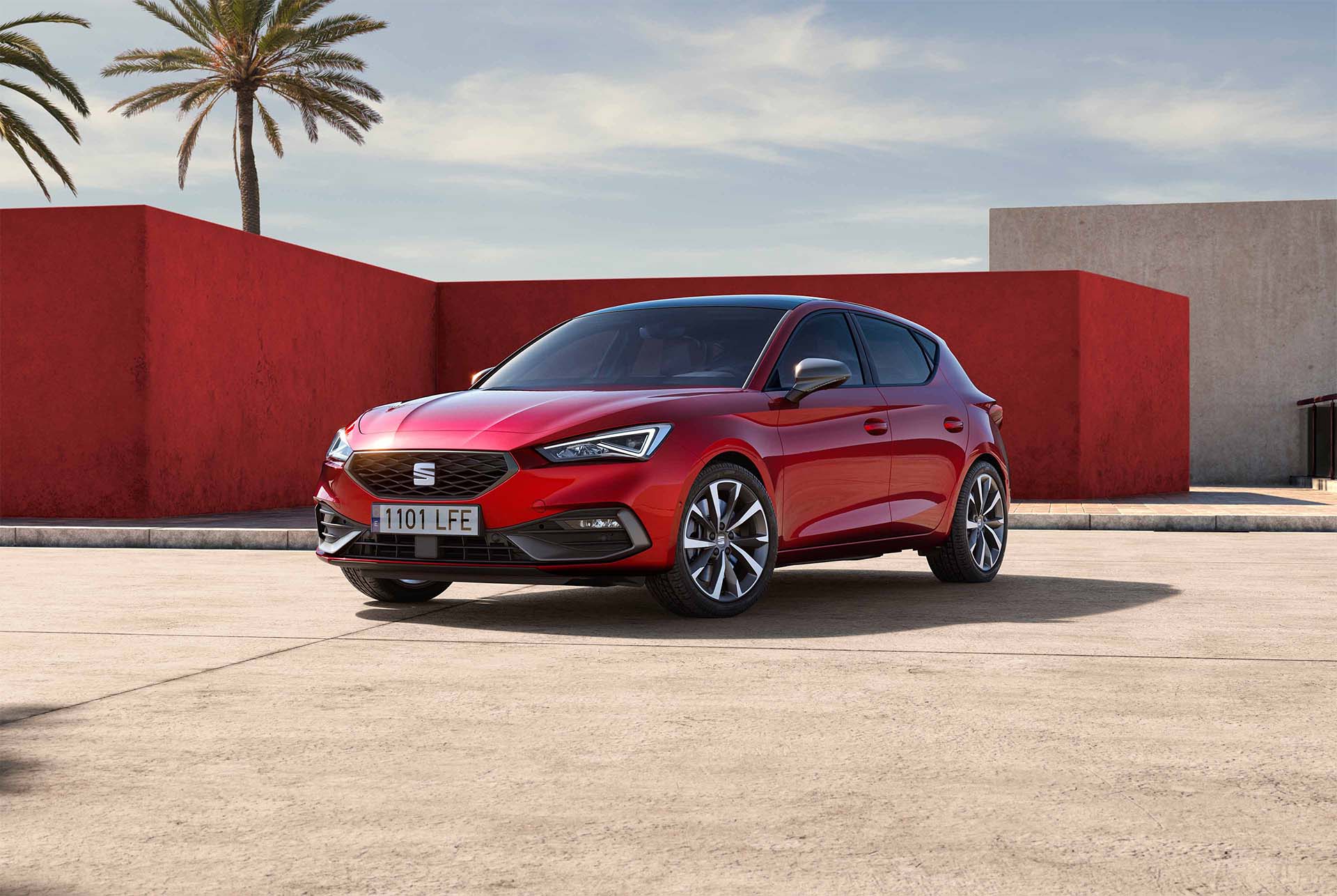 Une SEAT Leon 5 portes garée sur un parking, vue de trois quarts face devant un bâtiment en béton avec un grand escalier extérieur.