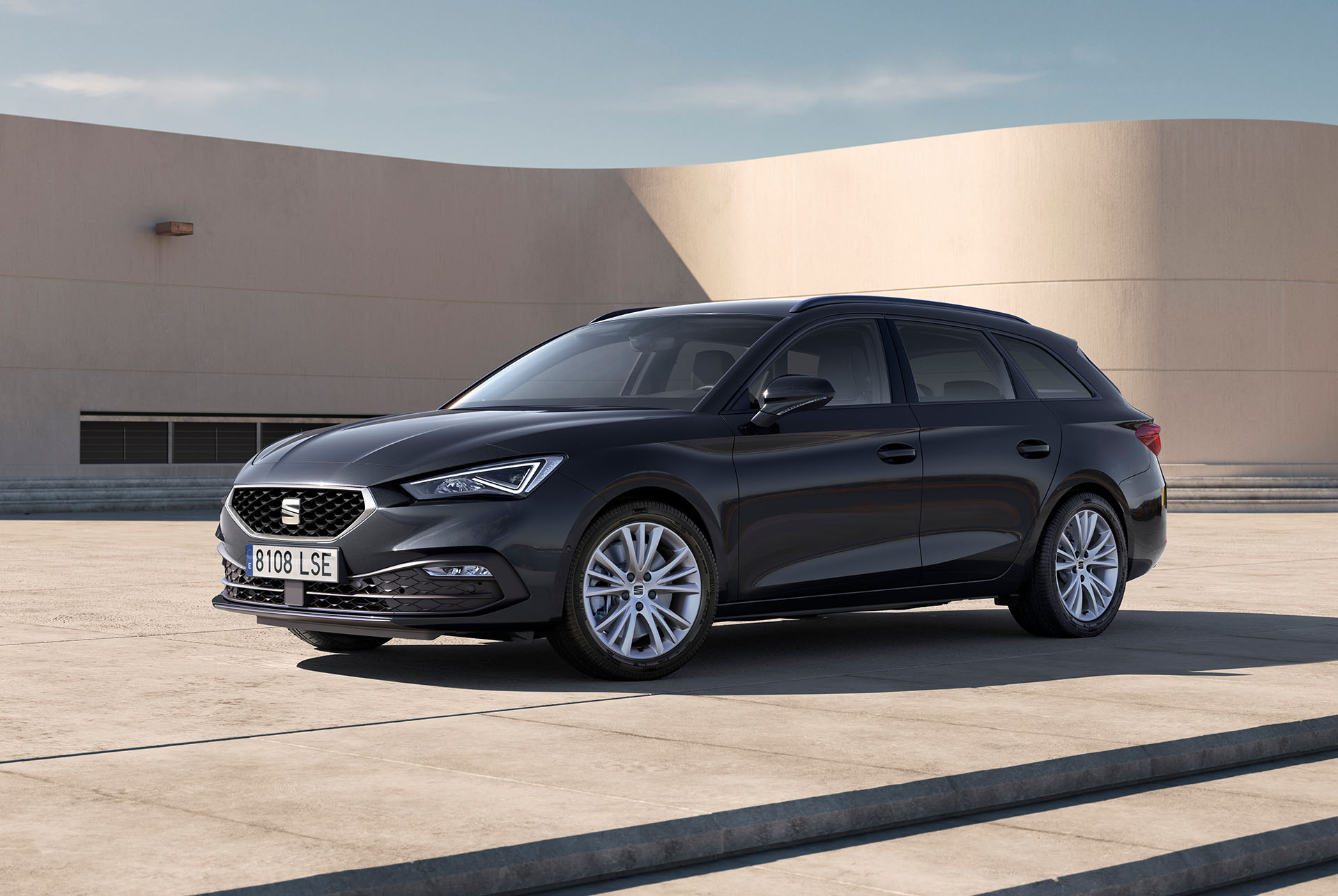 Un break SEAT Leon Sportstourer garé sur une esplanade en béton, vu de trois quarts face devant un bâtiment moderne aux murs courbes beiges.