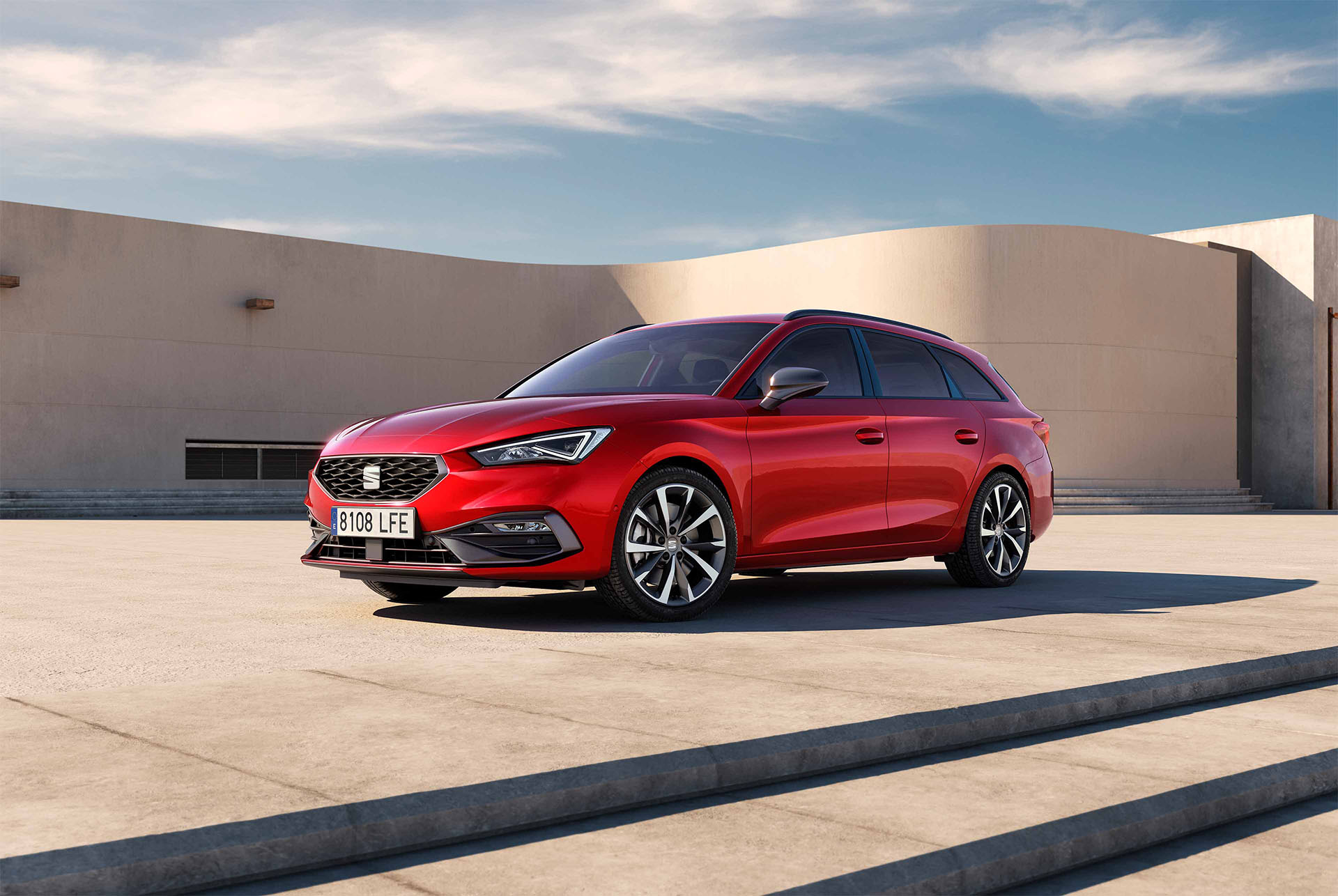 Un break SEAT Leon Sportstourer garé sur une esplanade en béton, vu de trois quarts face devant un bâtiment moderne aux murs courbes beiges.