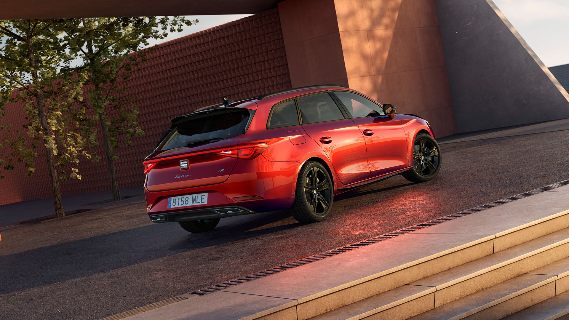 Vue de profil des rétroviseurs extérieurs noir brillant de la SEAT Leon Sportstourer FR, contrastant avec la carrosserie rouge, avec des éléments en béton en arrière-plan.