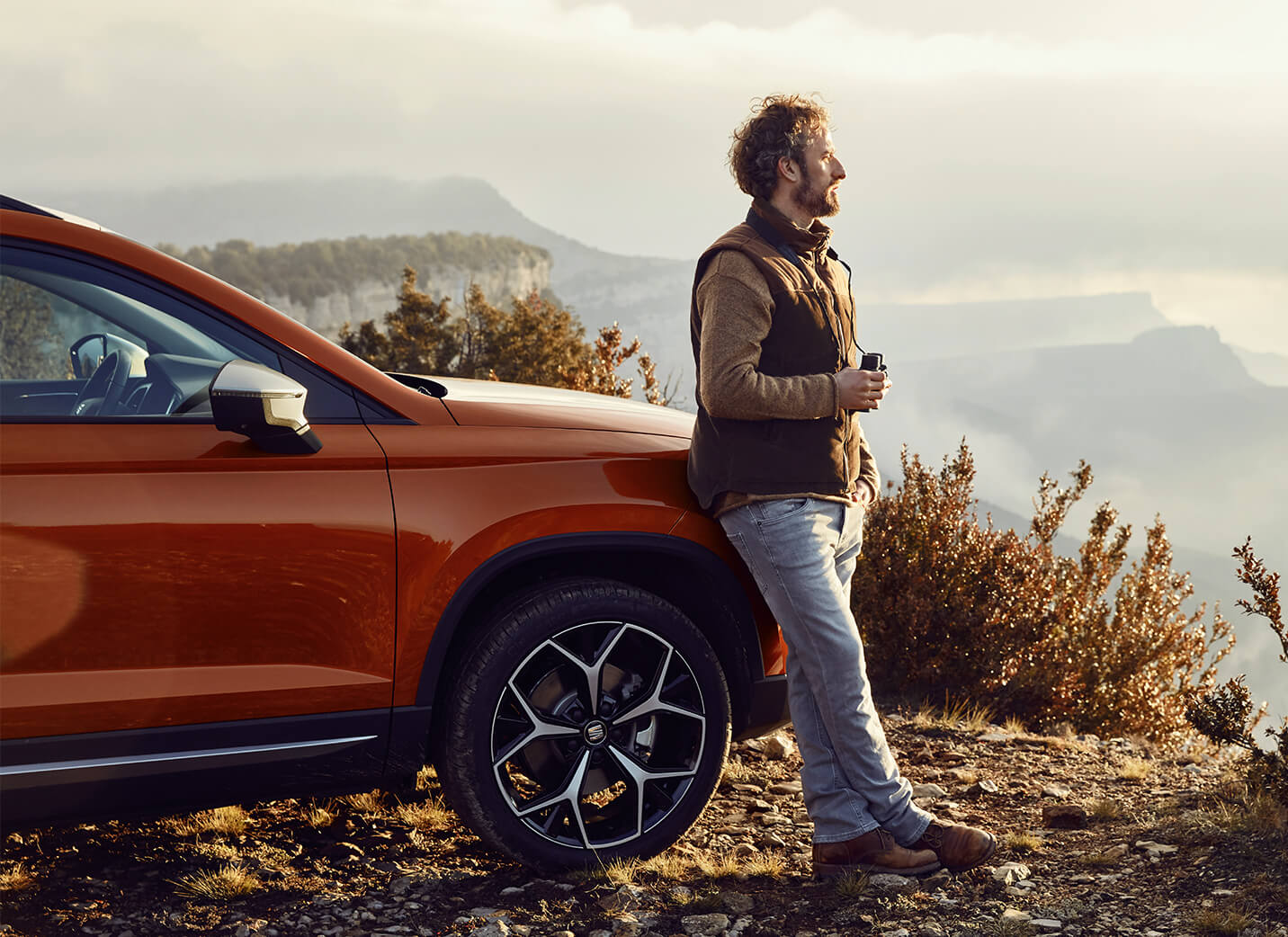 SEAT services de voitures neuves et d'entretien - SEAT Arona crossover SUV garé en surplomb d'une vallée avec un homme s'appuyant sur la voiture.